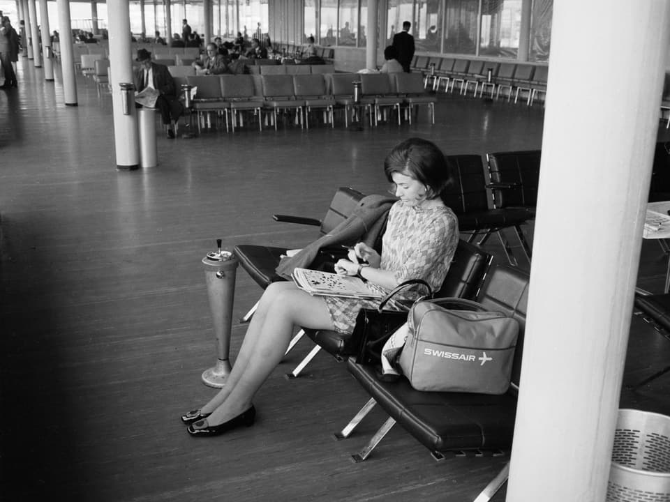 Eine Frau am Flughafen mit einer Swissair-Tasche. Das Bild ist schwarz-weiss.