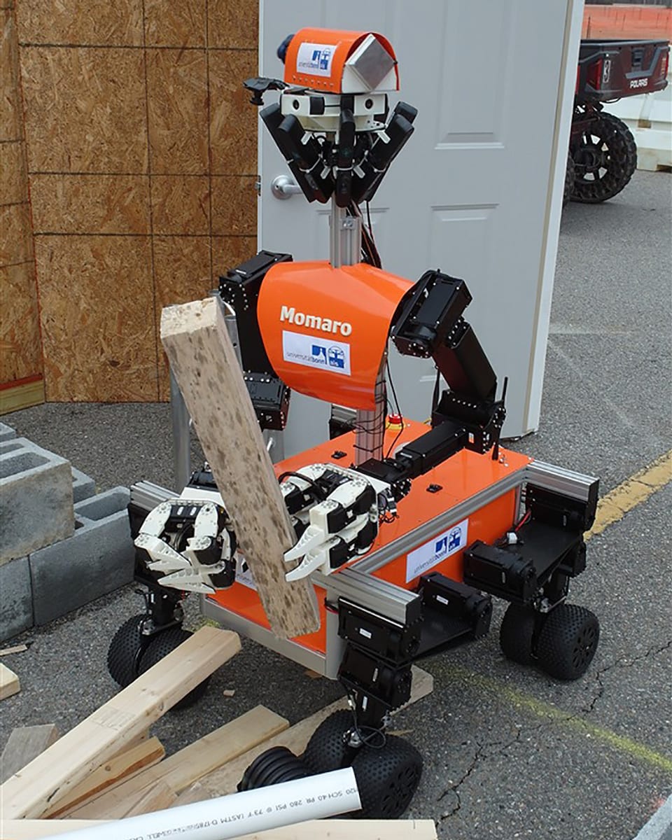 Ein Roboter mit Händen greift ein Holzstück und fährt dabei auf vier Doppelrädern.