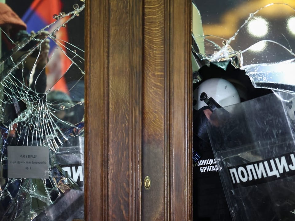 Polizisten sind hinter zerbrochenen Fensterscheiben im Belgrader Rathaus zu sehen.