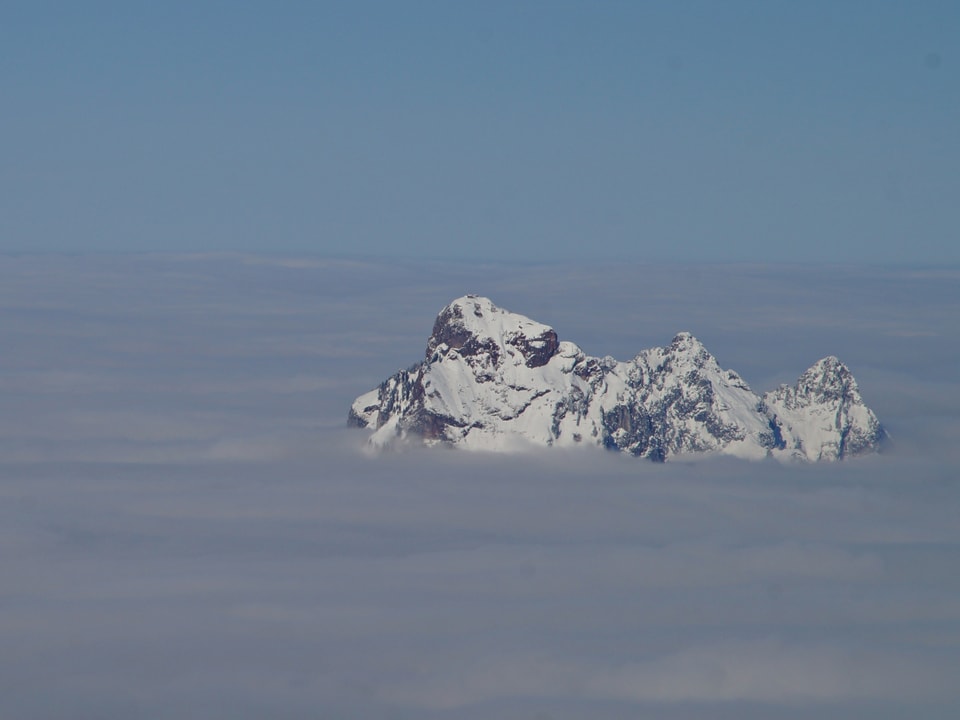 Nebelmeer mit nur einem Gipfel, der zu sehen ist. Er ist verschneit. 