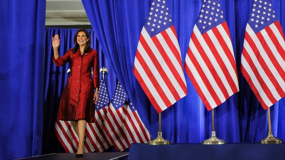 Nikki Haley tritt auf ein Podium und winkt. Im Hintergrund stehen US-Flaggen.