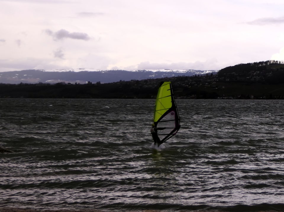 See mit leichten Wellen und Windsurfer bei grauem und nassem Wetter