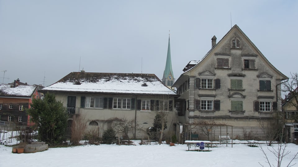 Ein altes Bauernhaus im Schnee, dahinter der Wädenswiler Kirchturm.