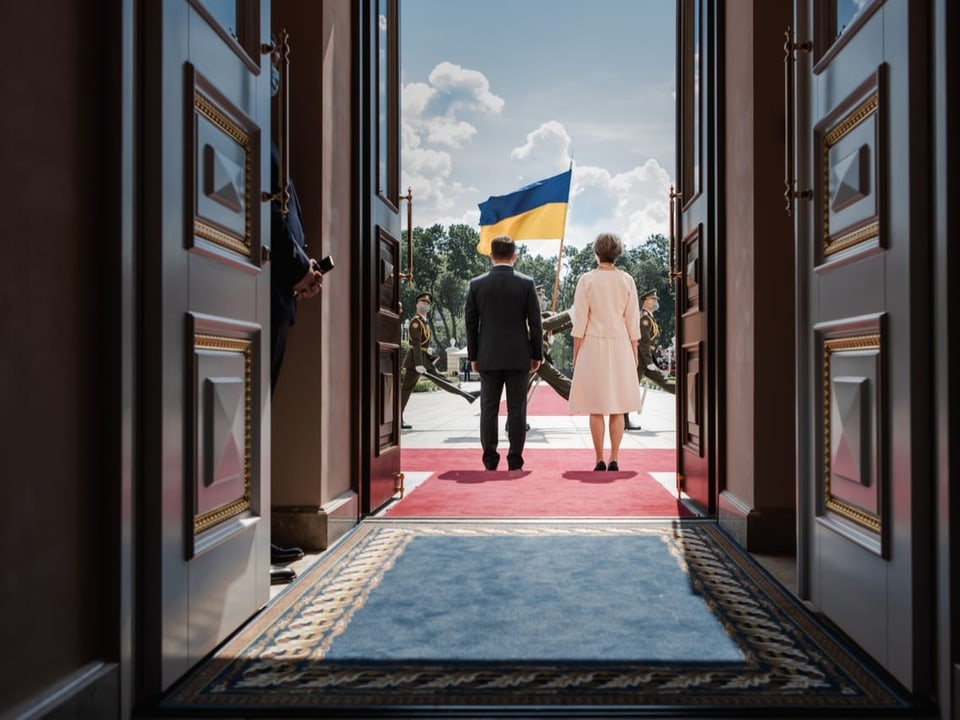 eine Frau und ein Mann stehen vor einem Gebäude, ukrainische Flagge im Hintergrund