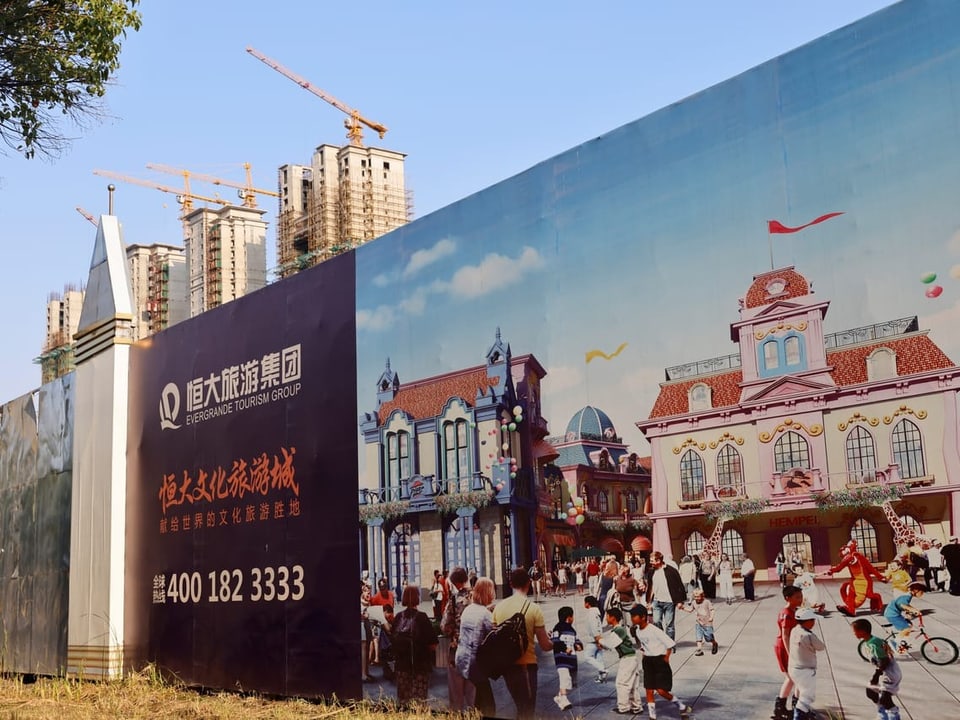 Ein Mauer beschreibt ein Bauprojekt in China. Im Hintergrund sind Rohbauten und Kräne zu sehen.