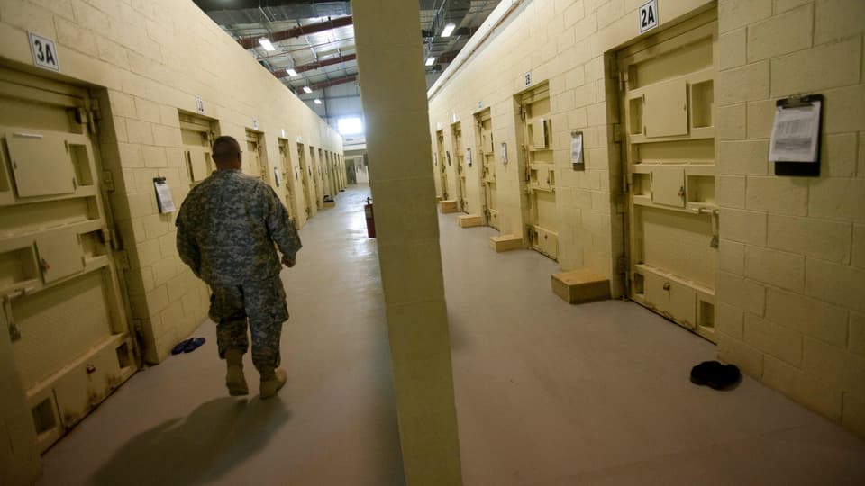 Ein US-Soldat geht durch einen gelben Gefängnisgang mit Zellen links un rechts.