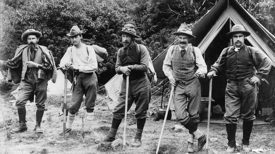 schwarzweiss-Foto von fünf Männern je mit Bickel und Hut, in Wanderschuhen und Stülpen. Aufgereiht vor Zelt.