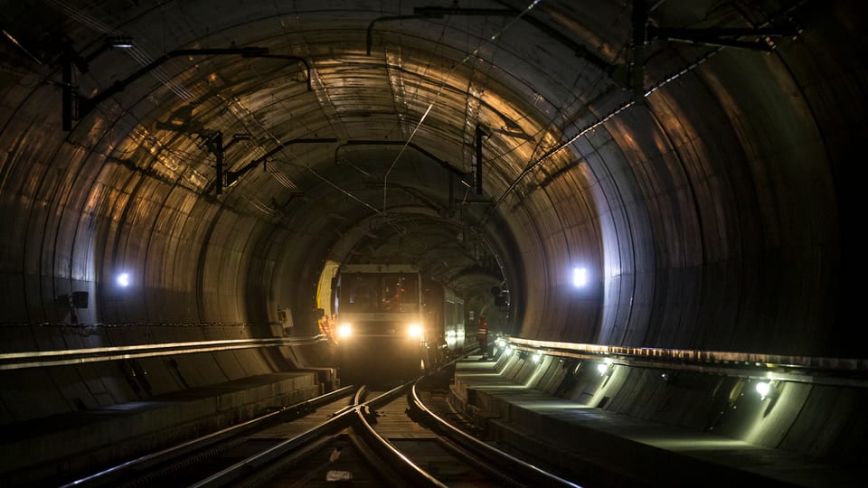 Blick in eine Röhre des Gotthard-Basistunnels, ein Zug mit eingeschalteten Scheinwerfern kommt entgegen