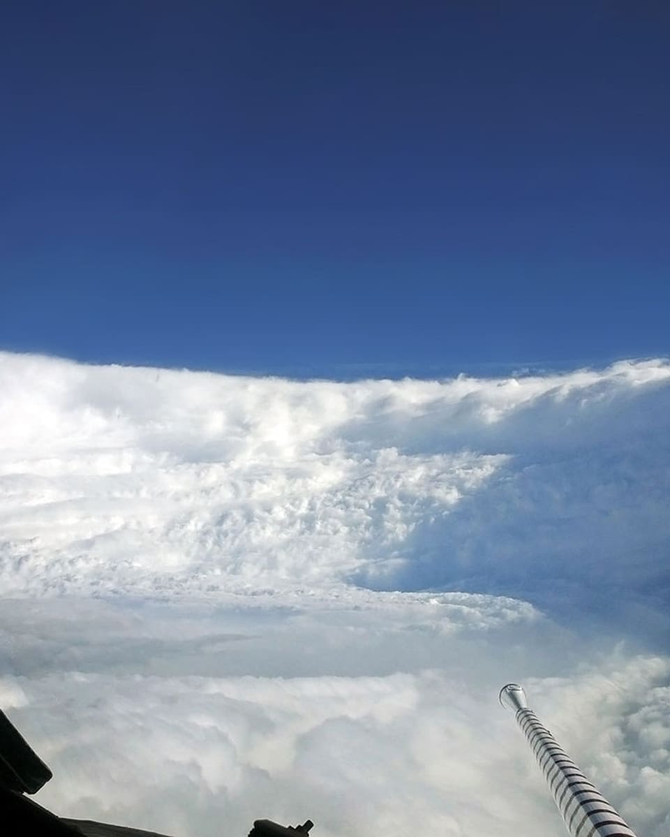 Wie in einem grossen, weissen Trichter fliegt das Flugzeug durch das Auge des Sturms. An den Seiten türmen sich senkrechte Wolkenwände. Darüber stahlblauer Himmel.