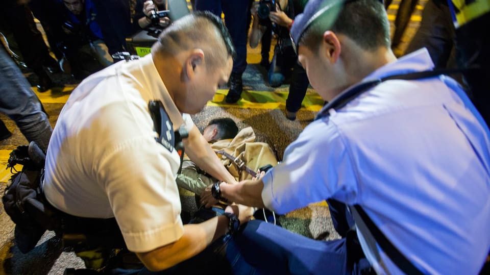 Polizisten legen einem Demonstranten Handschellen an