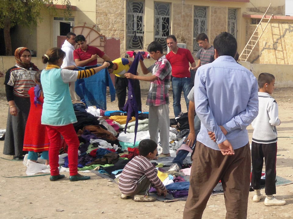 Flüchtlinge stehen vor einem Haufen Kleider und suchen sich passende Stücke heraus.