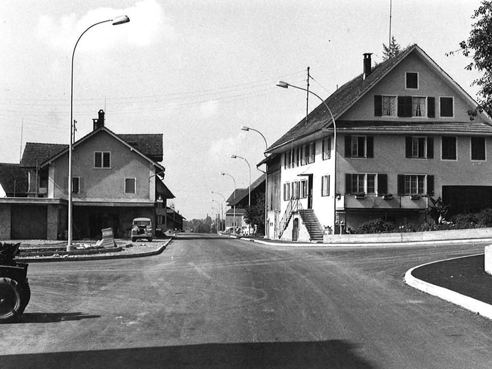 Schwarz-Weiss Fotografie von einer Strassenkreuzung mit Häusern rechts und links.