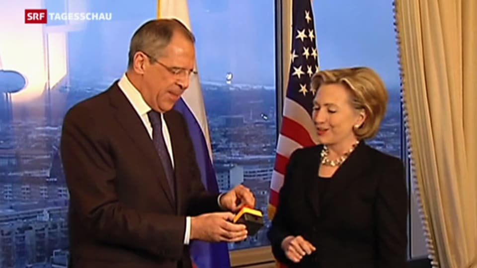 Sergej Lawrow hält freudig einen Schalter mit rotem Druckknopf in der Hand. Neben ihm steht Hillary Clinton.