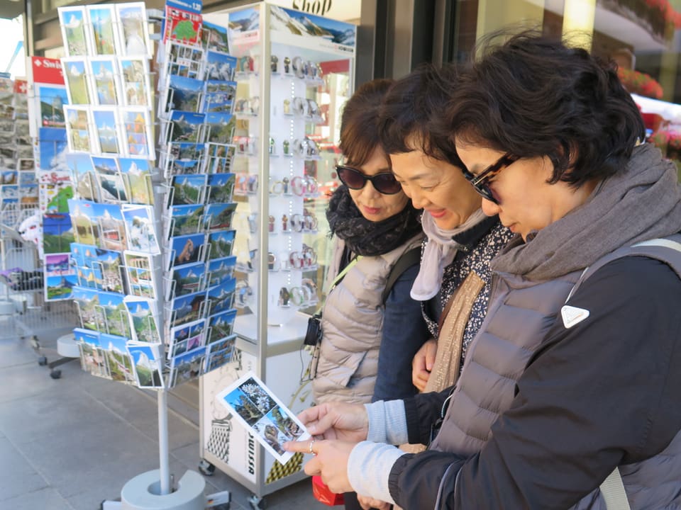 Ausländische Touristen kaufen eine Postkarte mit Murmeltier und Matterhorn.