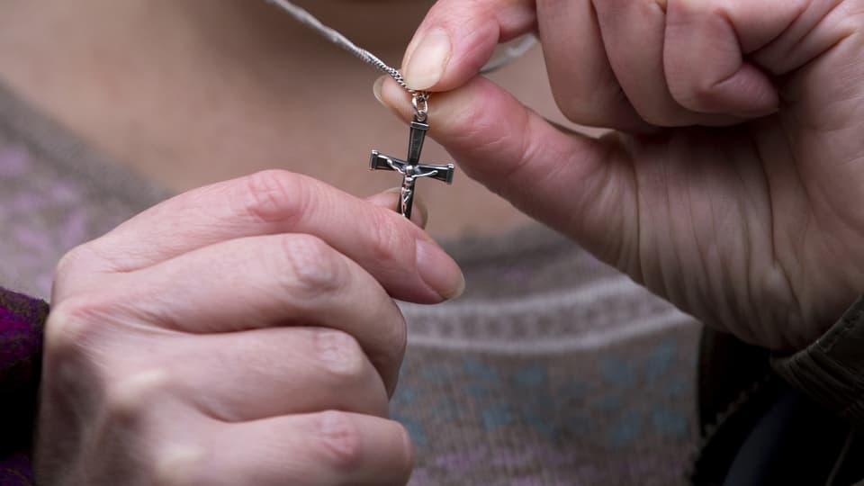 Eine Frau zeigt ihre Kruzifix-Halskette in eine Kamera.