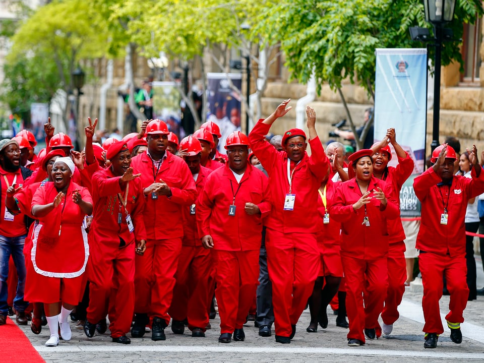 Gruppe von Mitglieder der Opposition in roter Arbeitskleidung auf Strasse gehend