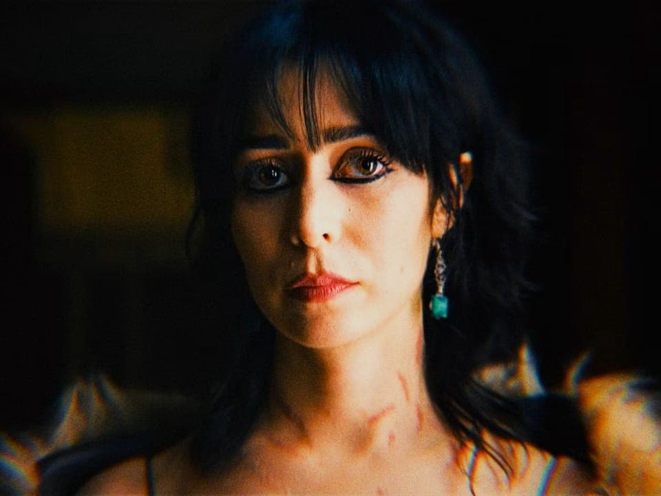 Close de Cristin Milioti com cabelos escuros e brincos azuis. Ela olha pensativamente para a câmera.