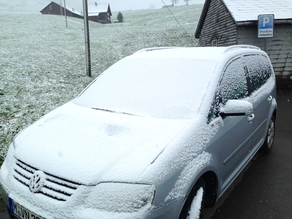 Aufnahme eines Personenwagens, der von Neuschnee bedeckt ist. Ebenso die Wiese im Hintergrund.