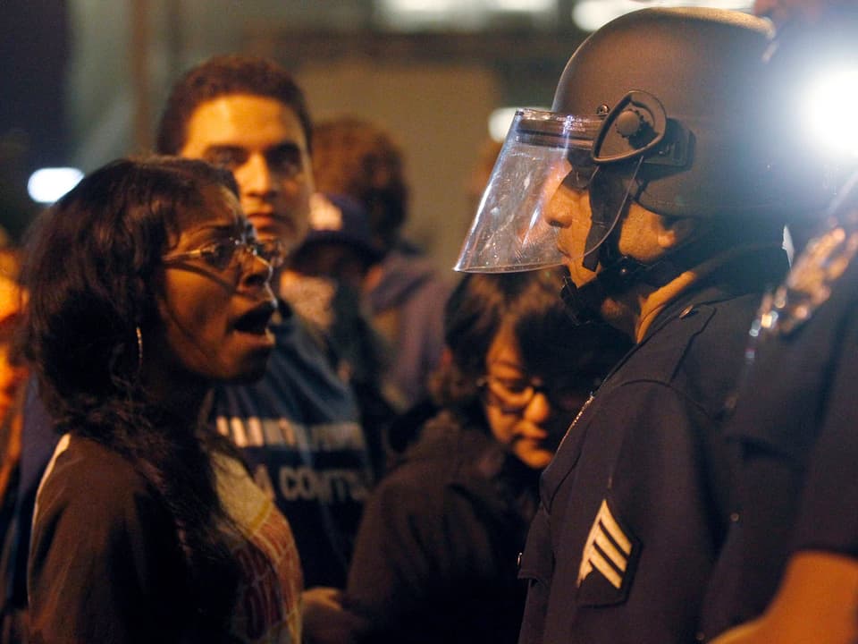 Eine Afroamerikanerin spricht mit einem weissen Polizisten in Kampfmontur.