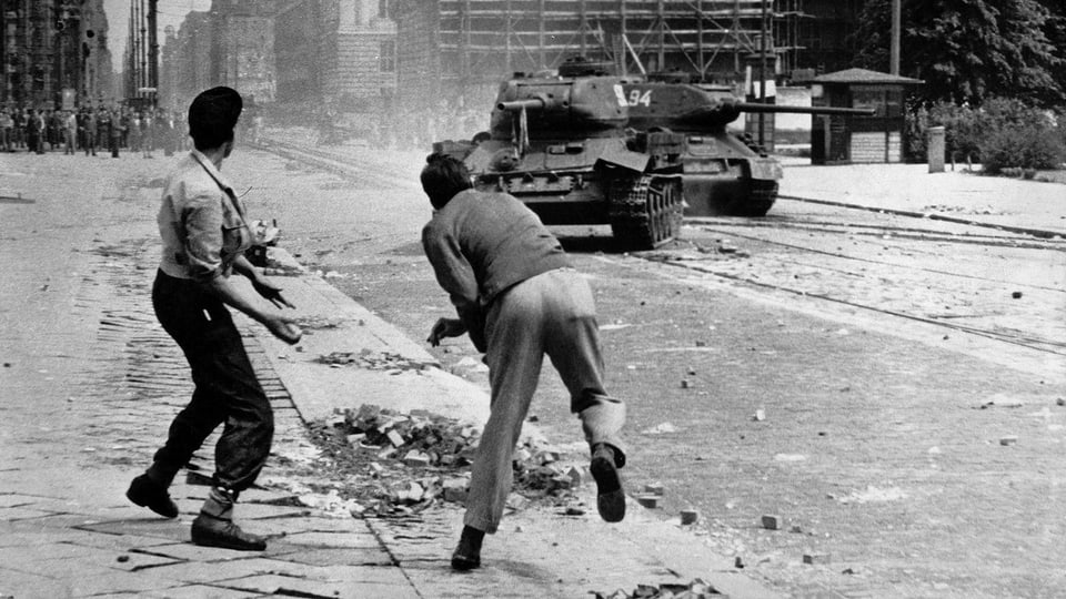 Zwei Männer werfen Steine auf einen sowjetischen Panzer. Schwarz-Weiss-Fotografie