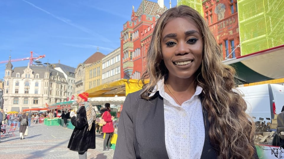 Dunkelhäutige Frau mit langen Locken, im Hintergrund Marktstände, ein Platz.