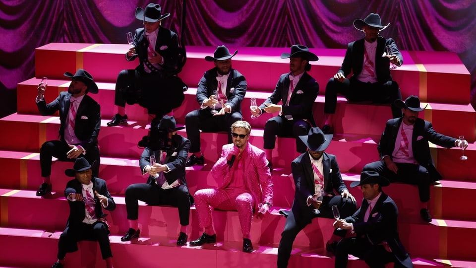 Ryan Gosling im pinken Anzug sitzt auf einer pinken Treppe gemeinsam mit Tänzern in schwarzen Anzügen und Cowboyhüten.