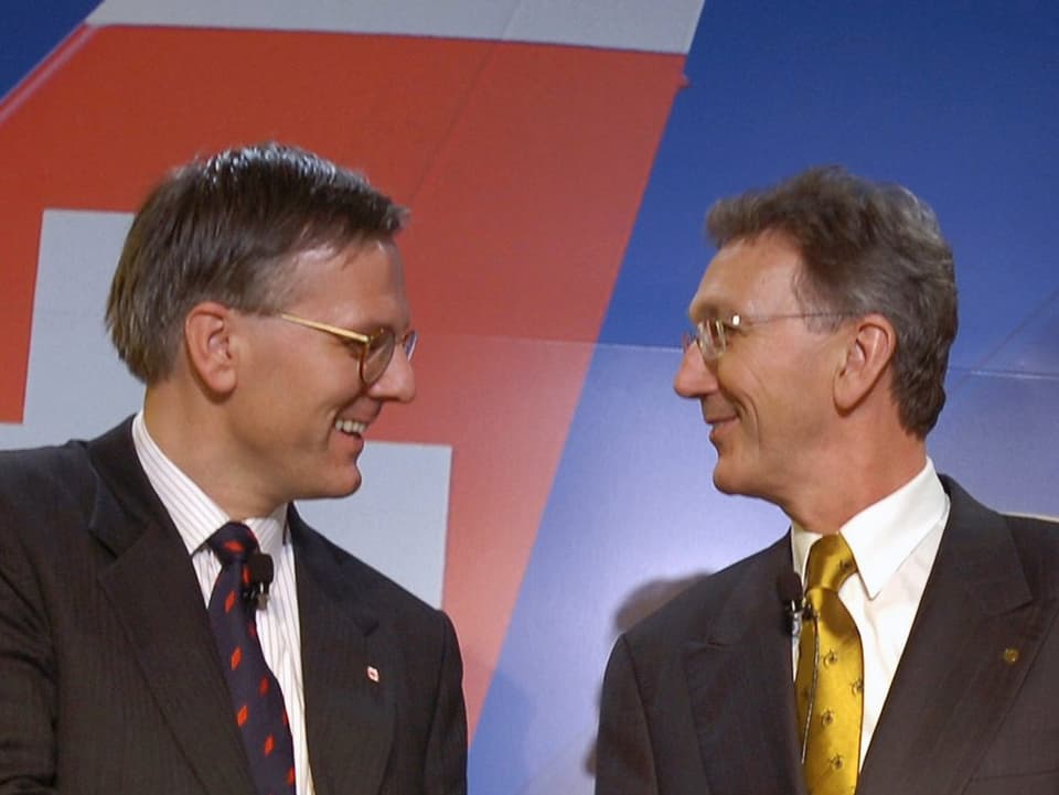 Die beiden Politiker gucken sich an. Im Hintergrund das Bild der Heckflosse einer Swiss-Maschine.