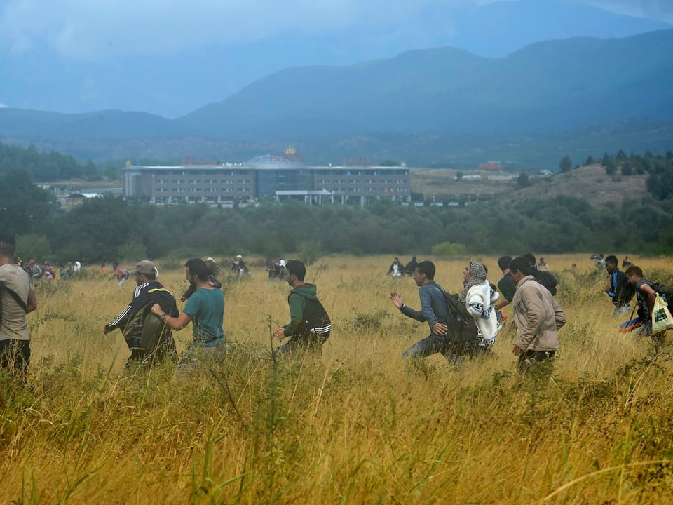 Flüchtlinge rennen über ein Feld, nachdem sie eine Absperrung durchquert haben 