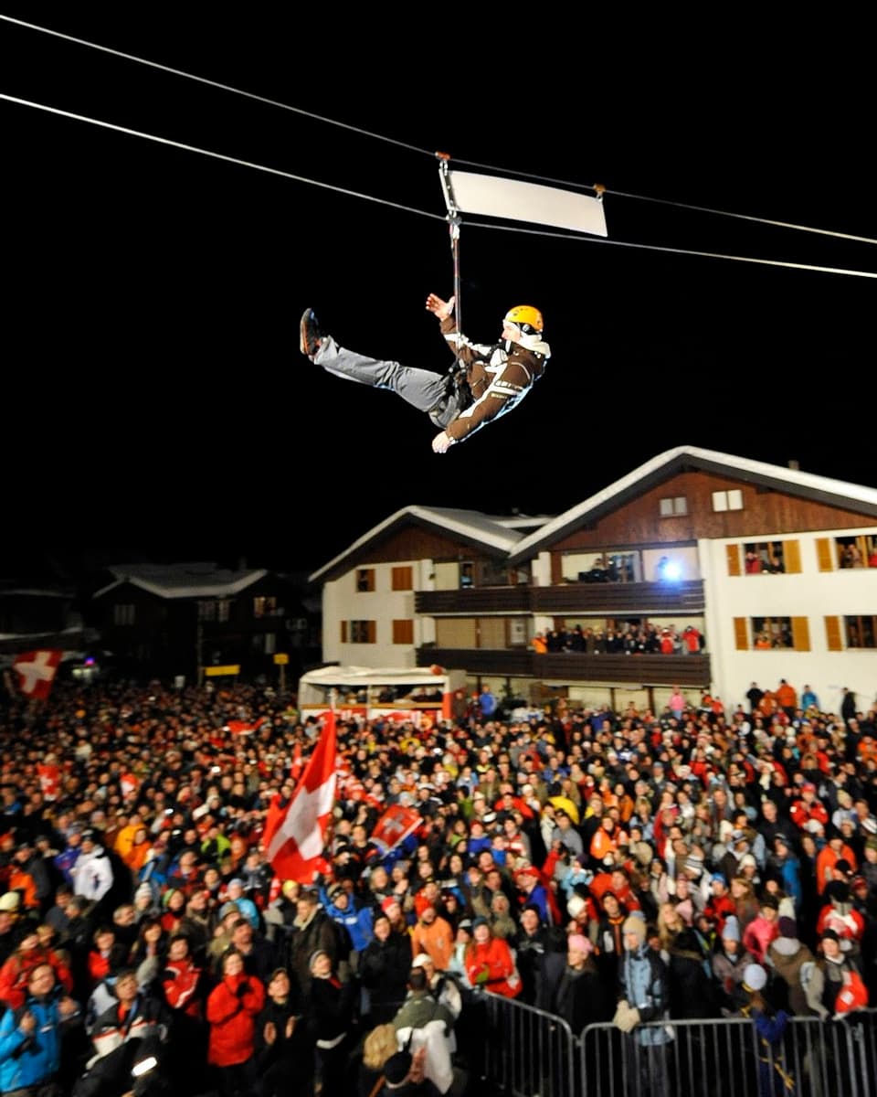 Skirennfahrer wird an einem Seil auf die Bühne gelassen. 
