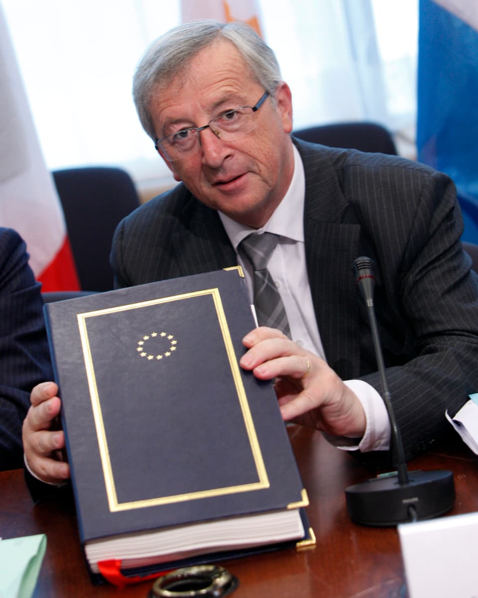 Juncker hält ein Buch in den Händen, auf dem die EU-Sterne abgebildet sind.