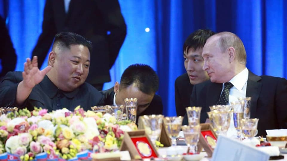 Kim Jong-un lacht und freut sich, Putin grinst auch. Dahinter zwei Männer, vermutlich Sicherheitsleute