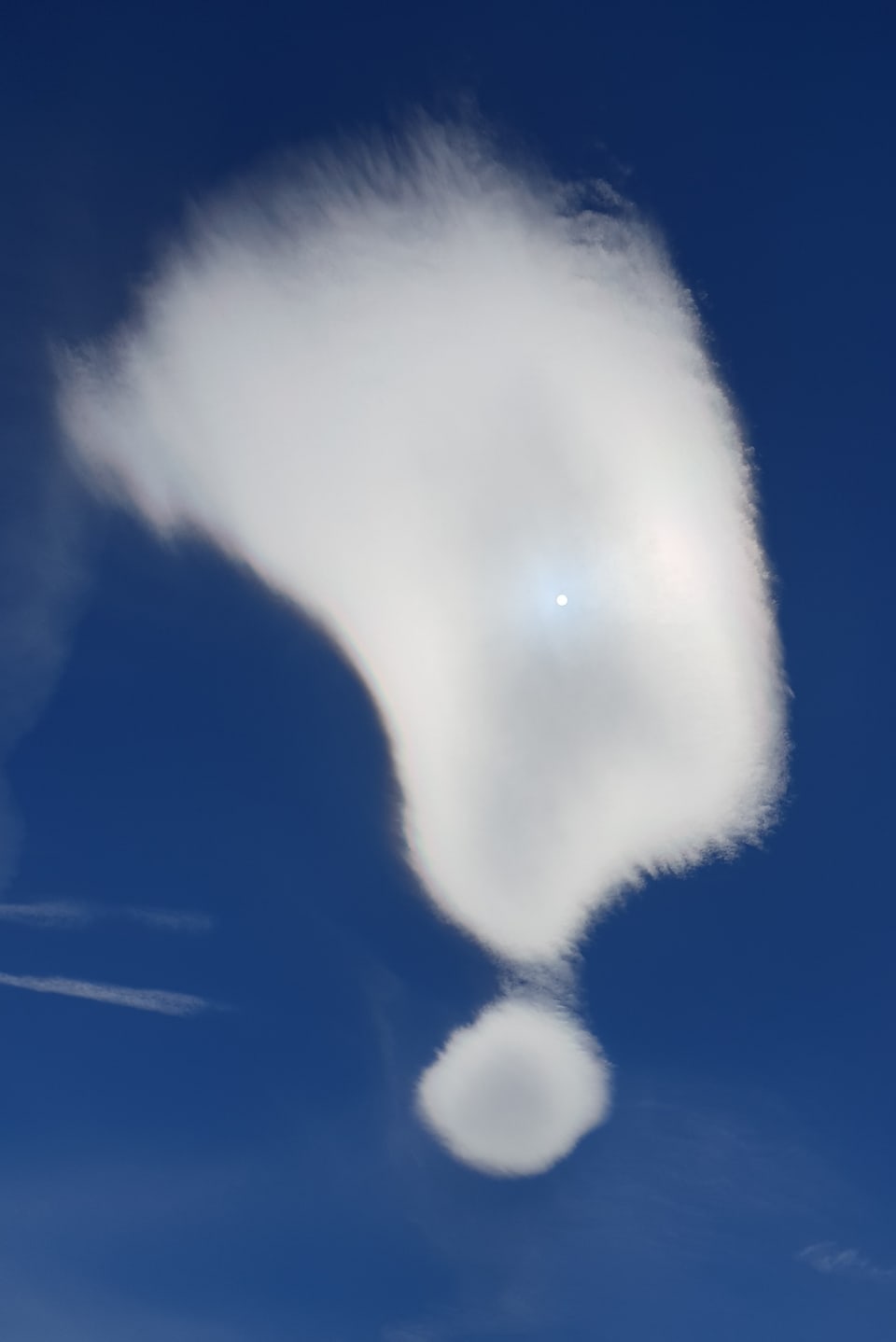 Wolken in Form eines Fragezeichens am stahlblauen Himmel. 