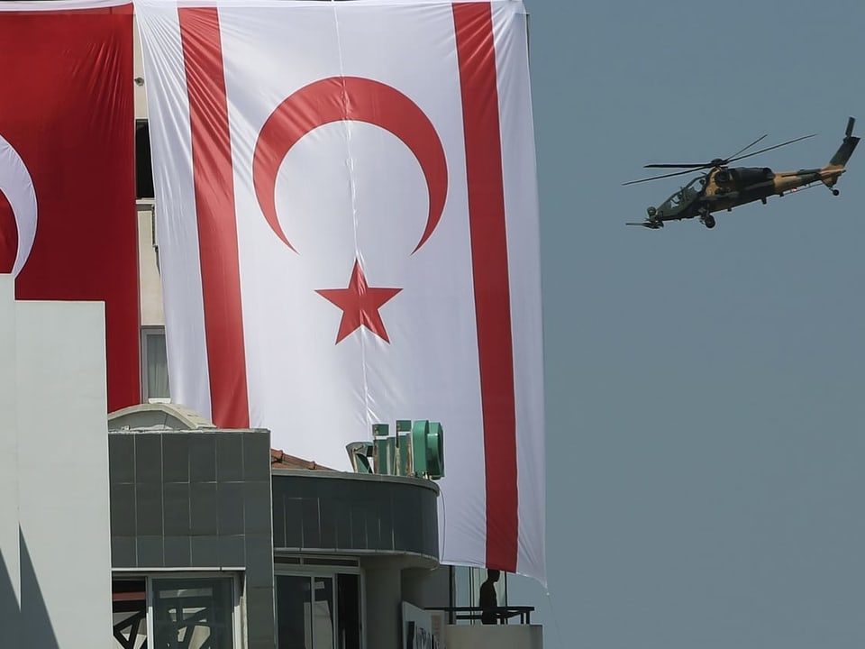 Ein Militärhelikopter fliegt über Nikosia. Im Vordergrund sind türkische Fahnen.