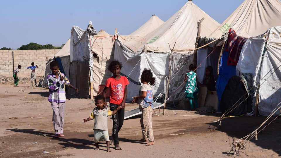 Kinder vor Zelten in einem Flüchtlingslager.