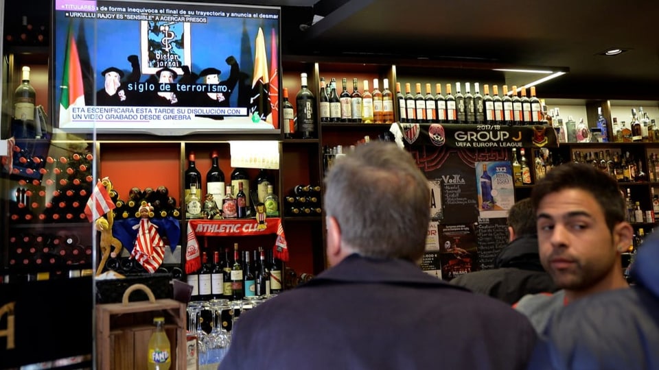 Zwei Männer in einer Bar sehen die ETA-Video-Botschaft in einem Fernsehbildschirm.