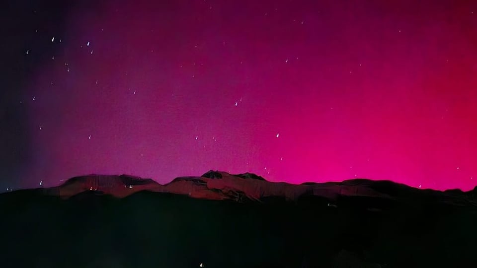 Bergsilhouette mit rosa Nordlichtern und Sternenhimmel.