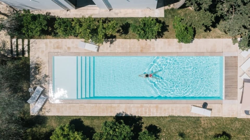 Bild aus der Vogelperspektive von einem Pool in einem Garten. Eine Frau schwimmt im Wasser.