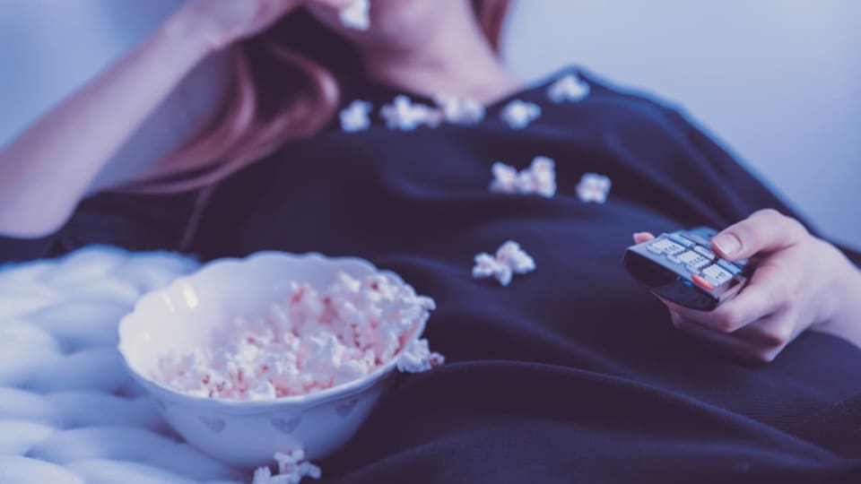 Eine Freu mit einer Fernbedienung in der Hand, isst Popcorn