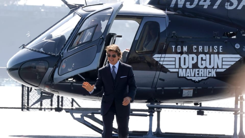 Ein Mann winkend vor einem Helikopter mit der Aufschrift «Top Gun».