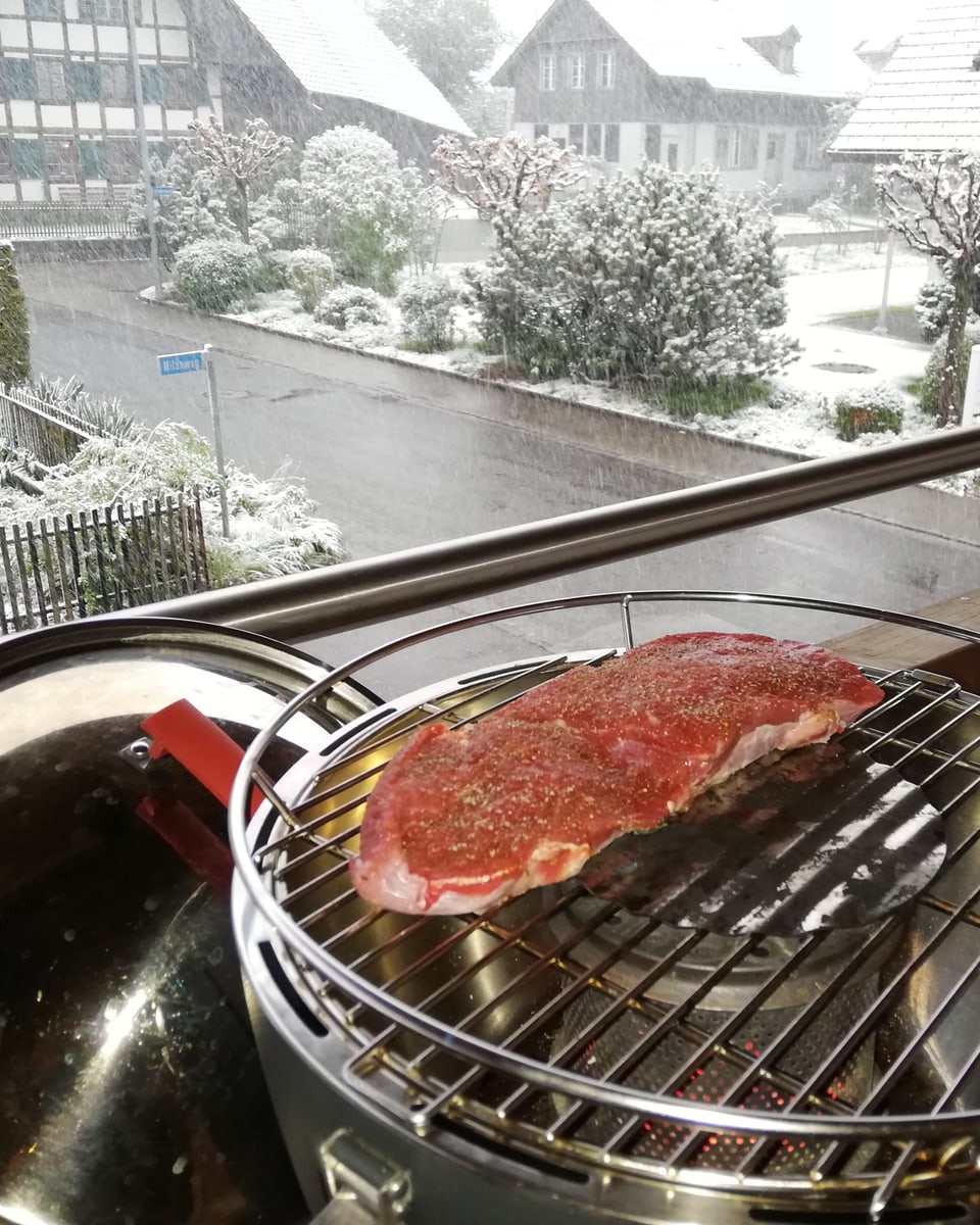 Balkonszene. Steak auf Grill. Dahinter sieht man, wie es schneit.