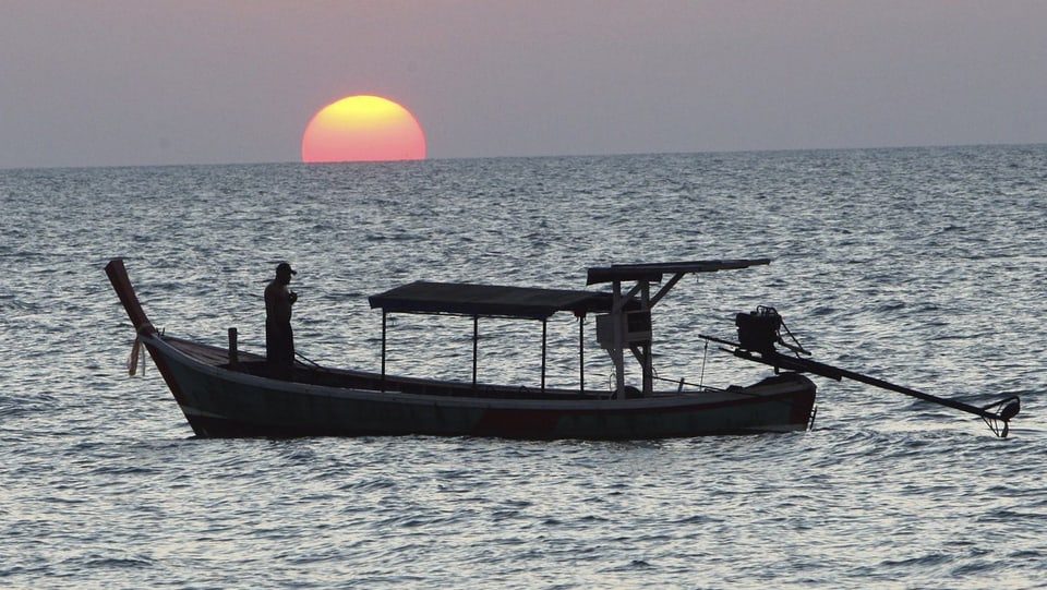 Ein Fischerboot vor der untergehenden Sonne.
