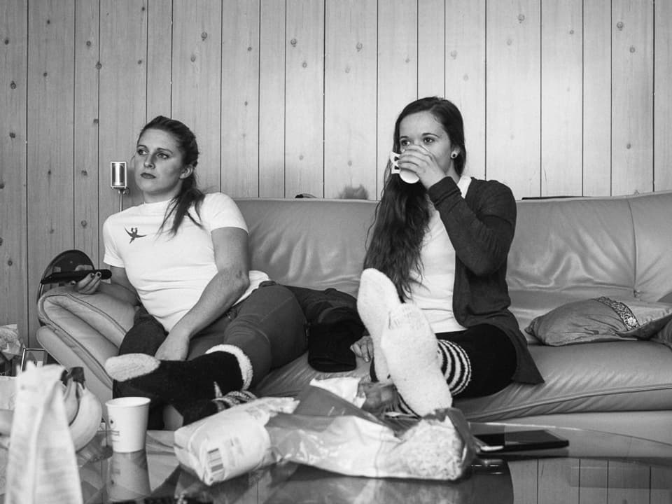 Jessica und Elise sitzen auf Sofa, schauen TV und schlürfen Tee