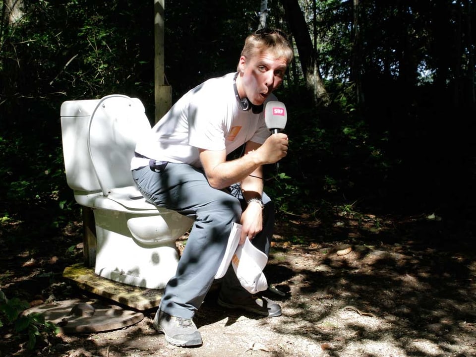 Reto Scherrer setzt sich auf eine Toilette, die mitten im Wald steht.