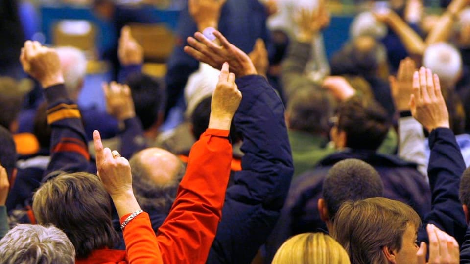 Leute erheben ihre Hand zur Abstimmung an einer Gemeindeversammlung