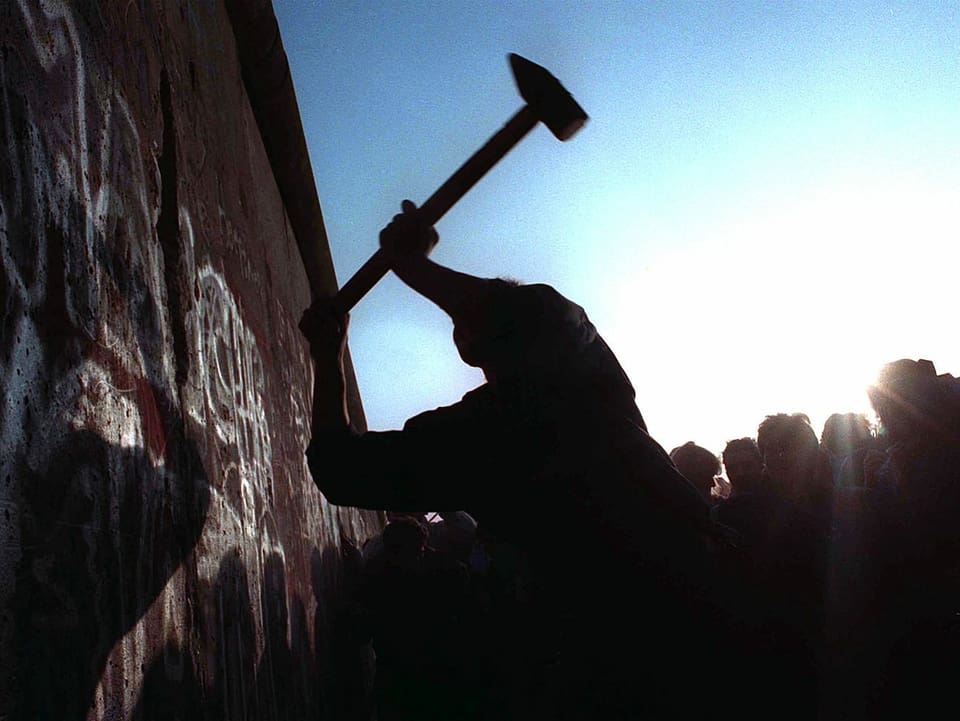 Ein Westdeutscher schlägt mit einem Vorschlaghammer auf die Berliner Mauer ein.