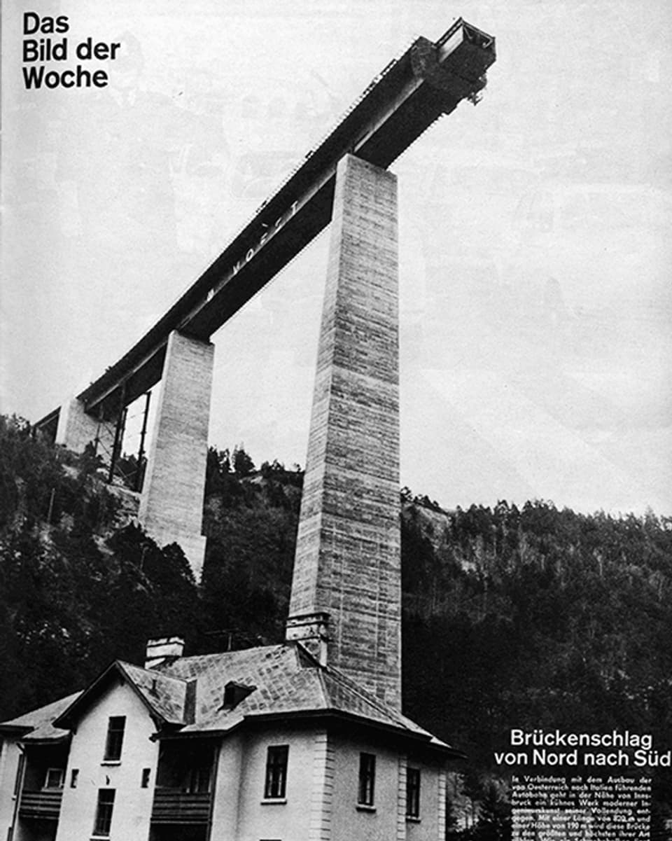 Auf einer schwarz-weissen Fotografie in einer Ansicht von unten eine halbfertige sehr hohe Brücke zu sehen.