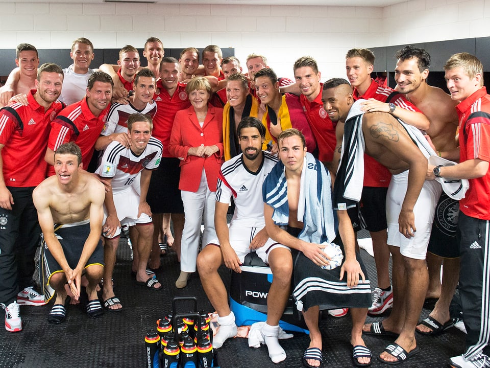 Angela Merkel inmitten von der deutschen Fussball-Nationalmannschaft in der Kabine.