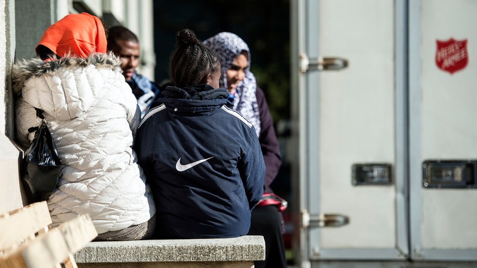 Asylsuchende sitzen auf einer Steinmauer eines Gebäudes. 