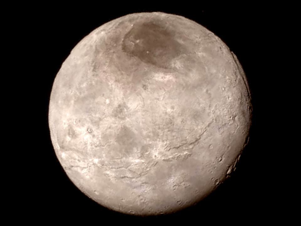 Nahaufnahme des Planeten Charon. In der oberen Polarregion ist eine dunke Fläche zu sehen.