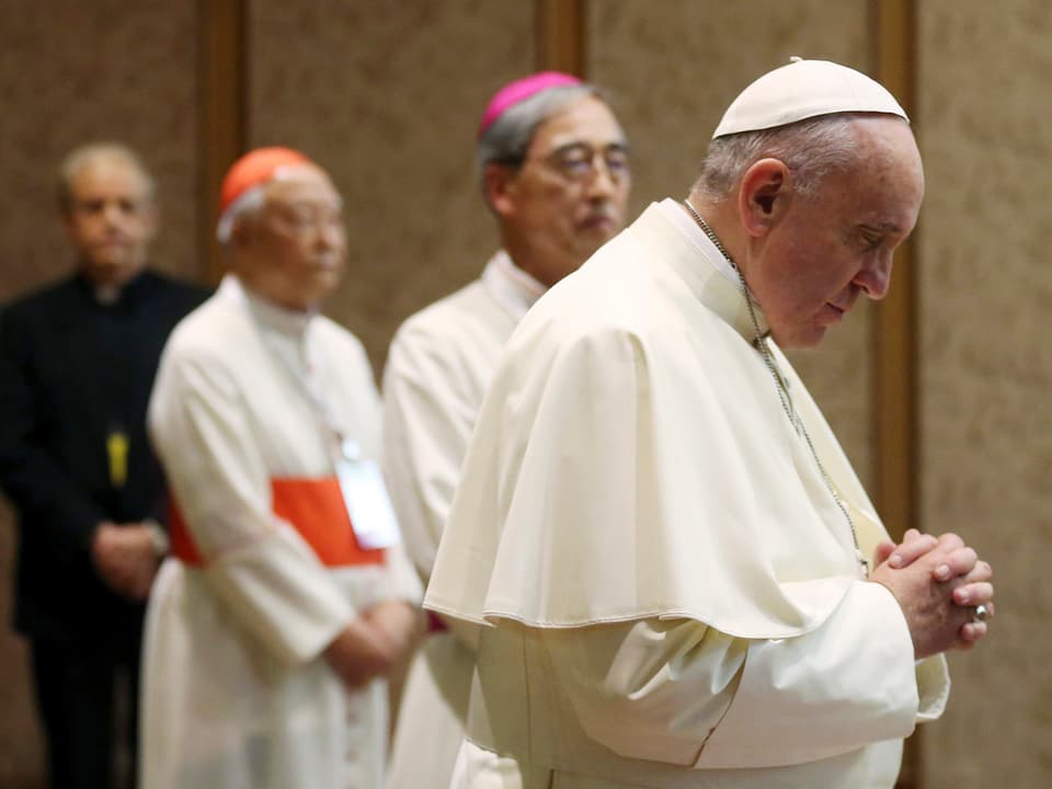 Der Papst betet, Geistliche im Hintergrund.